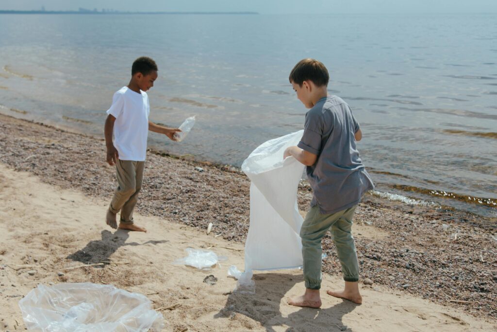 Two boys collect garbage at the beach, promoting volunteerism and environmental care.