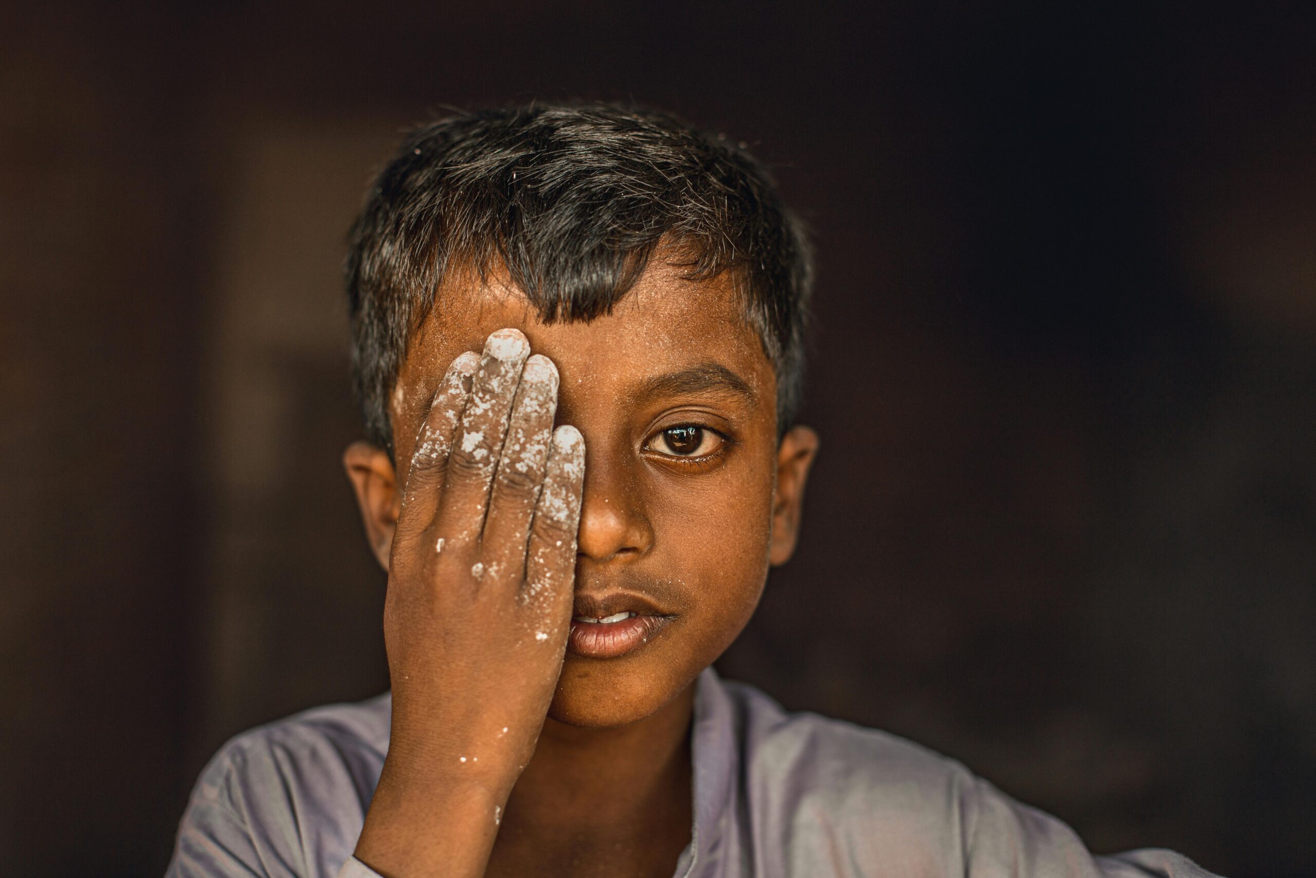 A thoughtful portrait of a child covering one eye with a hand, captured in Punjab, Pakistan.