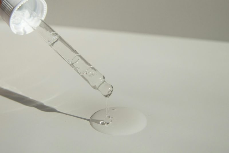 Close-up of a cosmetic pipette releasing serum onto a surface with soft sunlight.