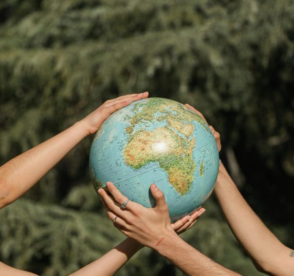 Four hands holding a globe outdoors, symbolizing unity and environmental conservation.